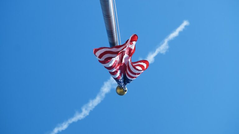 Flaga USA na maszcie, w tle ślad samolotu